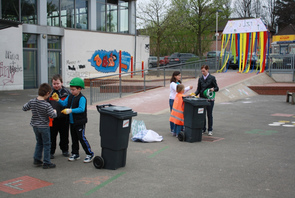 Wir sehen Kinder bei der Müllrallye auf dem Schulhof. Im ersten Schritt muss Müll getrennt werden.